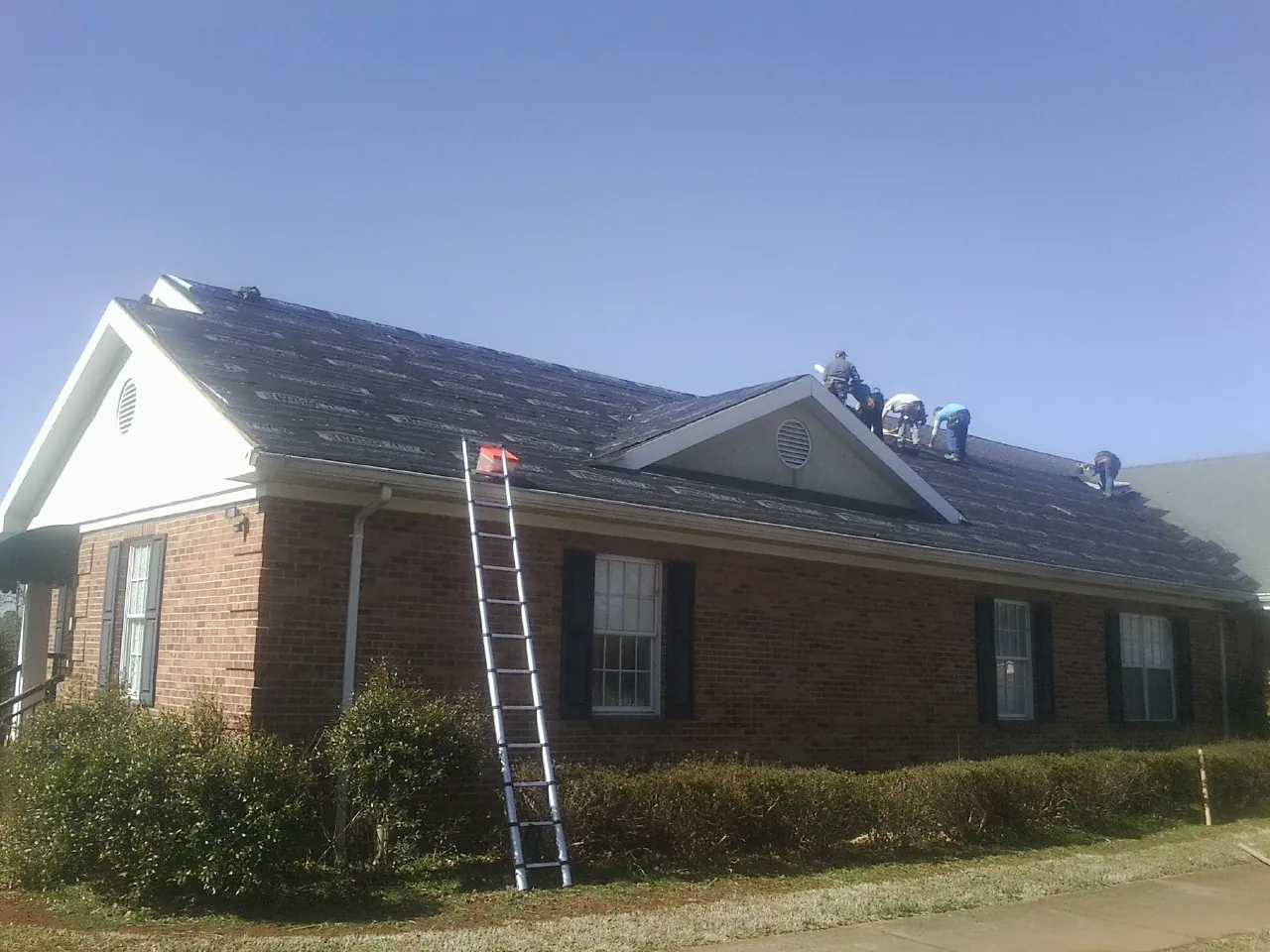 Crew tearing shingles off a brick ranch roof with a ladder set — Emergency Roof Repair work by our crew in Livermore